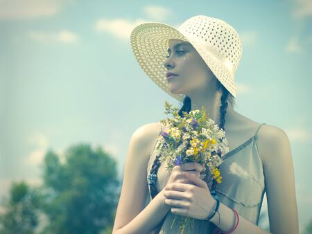 Summer day on the meadow, beauty female portrait. Young girl walking with wild flowers bouquetの写真素材