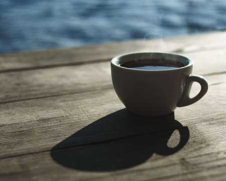 Morning on the river bank. A cup of delicious aromatic coffee on the tableの写真素材