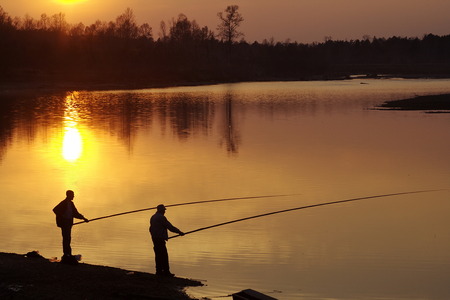 Silhouettes of two fishers on night riverの写真素材