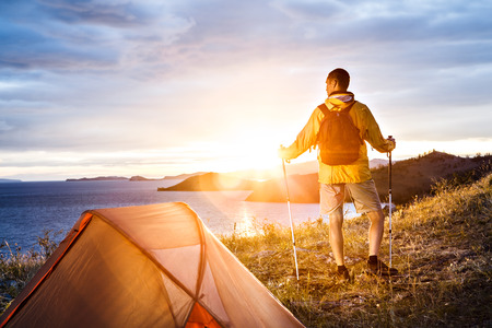 Backpacker looking at beautiful sunrise at big lake near tentの写真素材
