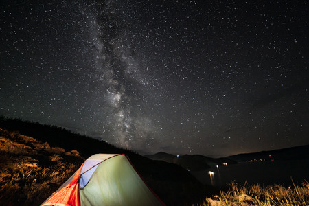 Illuminated tent at night under night stars.