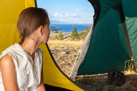 Young woman sitting into the tent and looking through open doorの写真素材