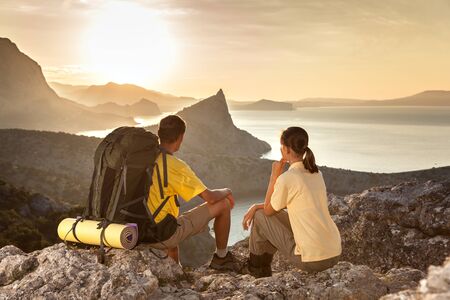 Couple is hiking a mountain and looking at the sunrise above the seaの写真素材