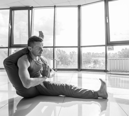 Athletic muscular young man working out, yoga, pilates, fitness training, doing side bend, asana Parighasana, Gate Yoga Pose, gray background, low key shotの写真素材