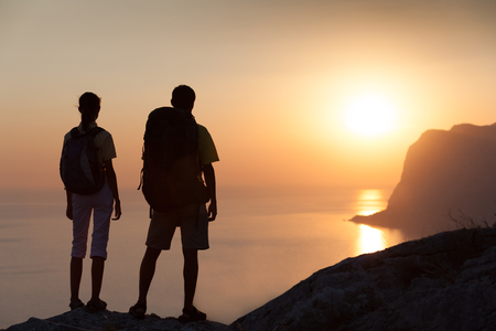 Couple hiking a mountain and looking at orange sunrise above the seaの写真素材