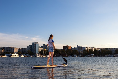 Young woman on Stand Up Paddle Board. SUP. Shape of a city on backgroundの写真素材