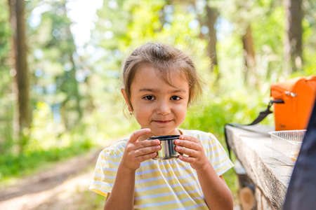 Cute little girl in a summer forest holding a cup of tea and smiling. walk to drink hot tea . Seasonal outdoor activitiesの写真素材