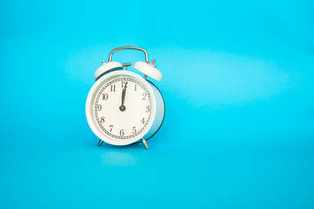 White alarm clock on a blue background. Free space for an inscription. Time conceptの写真素材