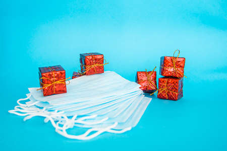 Blue medical face mask with New Year gifts isolated on light blue background. Beautiful stack of disposable medical masks on a blue background with red Christmas boxes. Place for textの写真素材