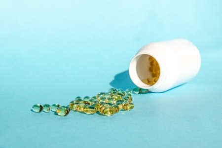 Vitamin medicinal capsules are poured from a white bottle on a blue background. Healthy lifestyle.の写真素材