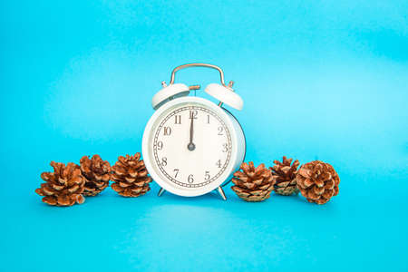 White alarm clock on a blue background. Free space for an inscription. Time concept. White alarm clock stands next to new year shiny conesの写真素材
