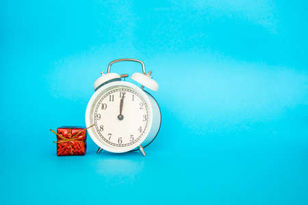 White alarm clock on a blue background. Free space for an inscription. Time concept. White alarm clock with small red new year gift boxの写真素材