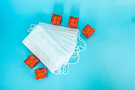 Blue medical face mask with New Year gifts isolated on light blue background. Beautiful stack of disposable medical masks on a blue background with red Christmas boxes. Place for textの写真素材