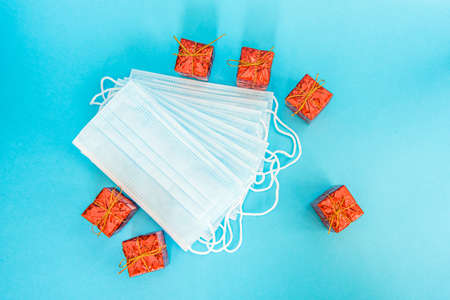 Blue medical face mask with New Year gifts isolated on light blue background. Beautiful stack of disposable medical masks on a blue background with red Christmas boxes. Place for textの写真素材