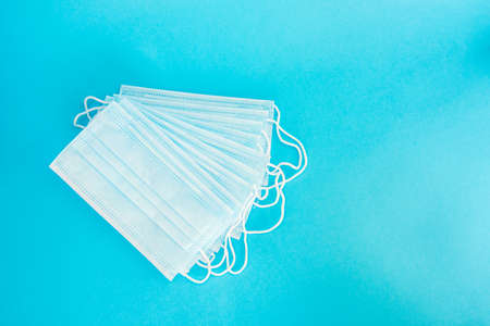 Blue medical face mask isolated on light blue background. A beautiful stack of disposable medical masks on a blue background. Place for textの写真素材