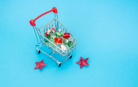 Small cart with a basket for purchases in the store on a blue background. miniature shopping basket with multi-colored Christmas stones.the camera is focused on the rocks. Place for your text.New yearの写真素材