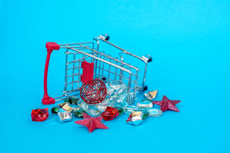 Small cart with a basket for purchases in the store on a blue background. miniature shopping basket with multi-colored Christmas stones.the camera is focused on the rocks. Place for your text.New yearの写真素材