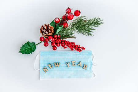 Green fir branches with red berries and Christmas decorations on a white background with a disposable protective mask. Merry Christmas or Happy New Year concept. Flat lay, top view, copy spaceの写真素材