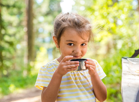 Cute little girl in a summer forest holding a cup of tea and smiling. walk to drink hot tea from a vaccum flask. Seasonal outdoor activitiesの写真素材
