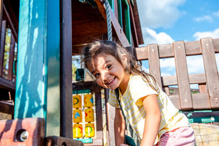 A little cheerful girl plays on vacation in the park on a children's playground. Happy child has fun on a swing in the park. Fun holidaysの写真素材
