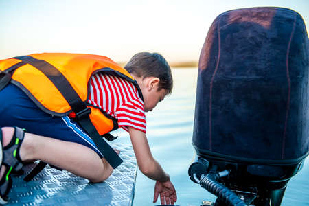 Happy boy 8 years old in a life jacket while walking on a boat. View from the back. Fun holidays on...