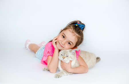 A little happy girl hugs a white cat of the British breed lying on a white background. Pets. Girl with cat on insulating white backgroundの写真素材