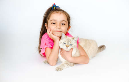 A little happy girl hugs a white cat of the British breed lying on a white background. Pets. Girl with cat on insulating white backgroundの写真素材