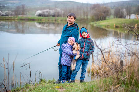 Happy family of three with a fishing rod on the river bank.の写真素材