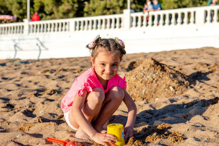 cute little girl playing with sand on the beach on summer vacationの写真素材
