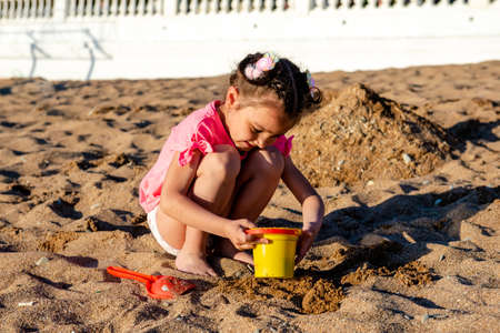 cute little girl playing with sand on the beach on summer vacationの写真素材