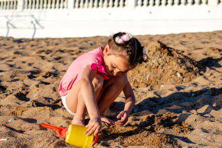 cute little girl playing with sand on the beach on summer vacationの写真素材