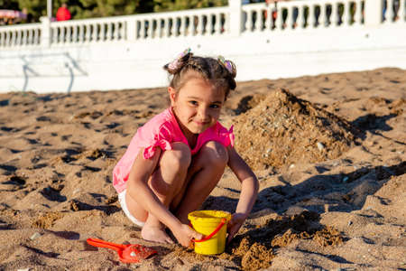 cute little girl playing with sand on the beach on summer vacationの写真素材