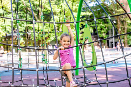 Little cheerful girl plays on vacation in the park at the playground. The child is having fun on the street on vacation. The child goes in for sports on simulators.の写真素材