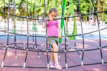 Little cheerful girl plays on vacation in the park at the playground. The child is having fun on the street on vacation. The child goes in for sports on simulators.の写真素材
