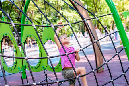 Little cheerful girl plays on vacation in the park at the playground. The child is having fun on the street on vacation. The child goes in for sports on simulators.の写真素材