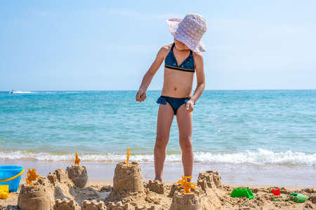 Girl playing on a sandy beach on summer vacation. A child is building a sand castle on the sea.の写真素材