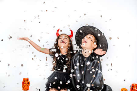two little girls in halloween costumes on a white background with confetti