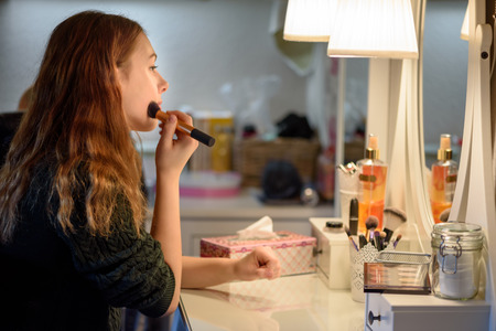 Young woman applying makeup cosmetics in front of a mirror at homeの写真素材