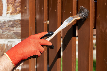 Painting wooden fence with a brown paint on a sunny dayの写真素材