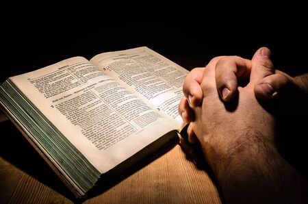 Hands placed on a bible, wooden table with dark backgroundの写真素材