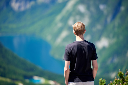 Young man standing on a mountain and looking to the valley bellow