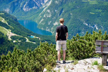 Young man standing on a mountain and looking to the valley bellowの写真素材
