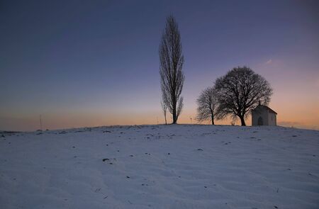 Sunset on frozen field with a chapel and cloudsの写真素材