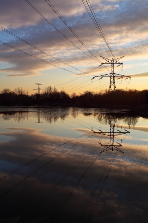 Electricity pylon with reflection in water at sunsetの写真素材