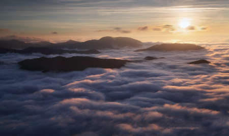 Sunset hidden behind clouds and fog over hills, bright yellow sun on colorful cloudscape, blue violet orange sky.の写真素材