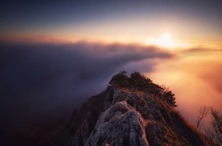 Sunset hidden behind clouds and fog over hills, bright yellow sun on colorful cloudscape, blue violet orange sky.の写真素材