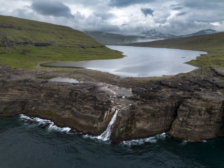 Waterfall and Cliffs of Traelanipa with the lake above the ocean, Faroe Islands, Denmark, Europe, aerial viewの写真素材