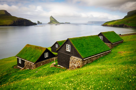 Tradicional faroese grass - covered houses in the village Bour. Drangarnir and Tindholmur sea stacks on background. Vagar island, Faroe Islands, Denmark. Landscape panoramaの写真素材