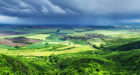 Summer storm clouds seen from a drone over a vast green forest and village with houses in a fairy tale landscape.の写真素材
