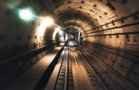 Long exposure captures the dramatic motion of a metro train moving through a tunnel. Bright lights...